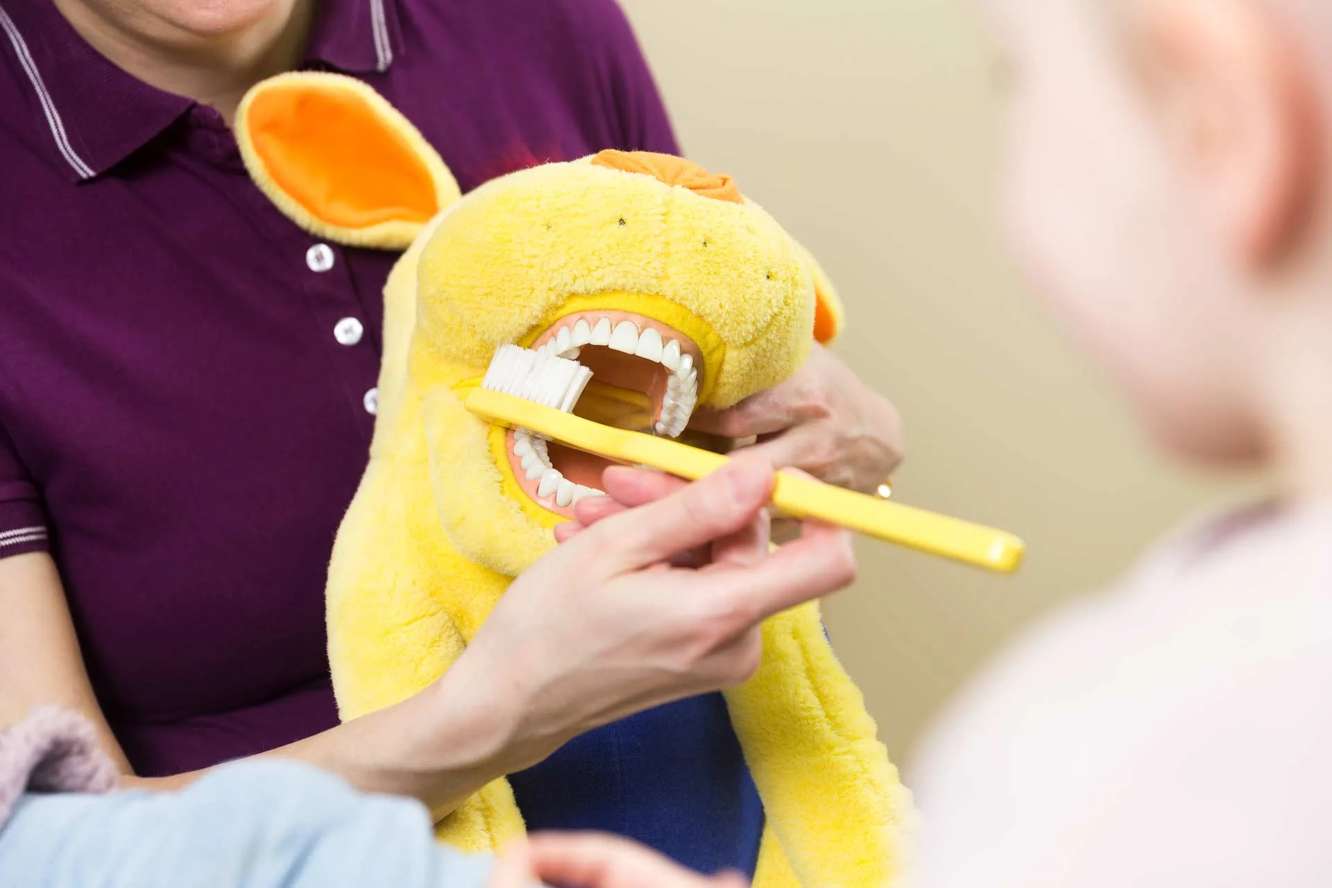 Zahnärztin zeigt einem Kind das korrekte Zähneputzen am Beispiel eines Kuscheltiers.